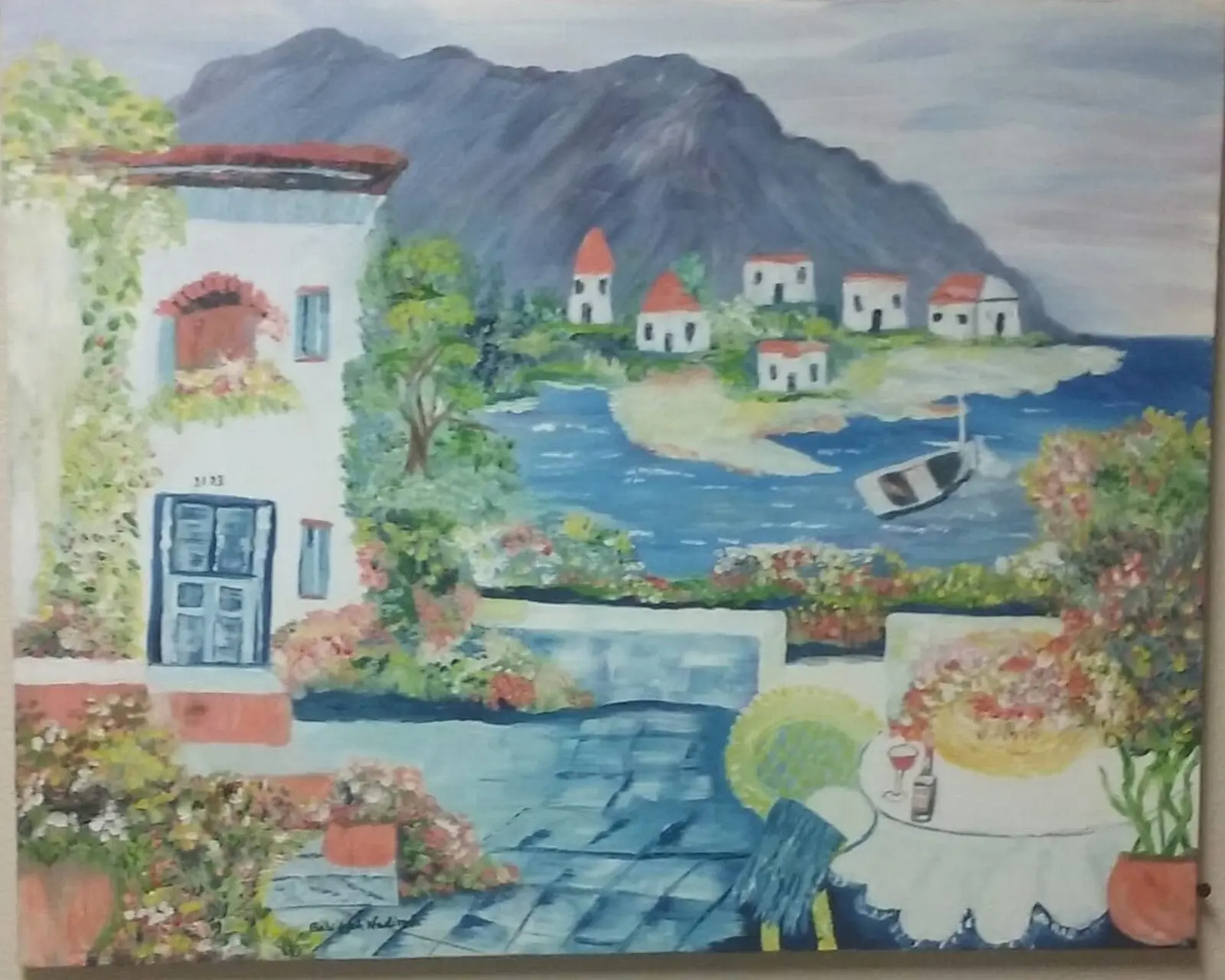 Painted coastal village with white buildings, a dark mountain, blue water, a small boat, flowers, and a terrace table.